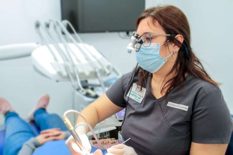 Una dentista con mascarilla y gafas de aumento atiende a un paciente en una clínica dental de Moratalaz. de Hospital Dental de Moratalaz "Martínez y Morcuende"