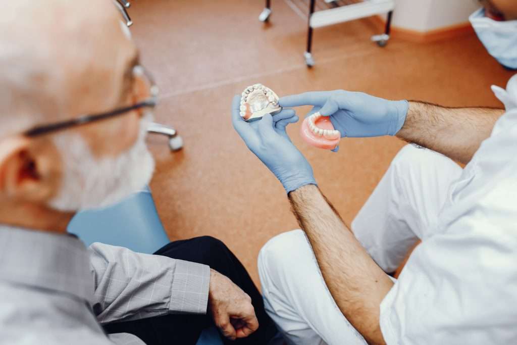 Un dentista en una clínica dental muestra un modelo dental a un paciente mayor durante la consulta. de Hospital Dental de Moratalaz "Martínez y Morcuende"