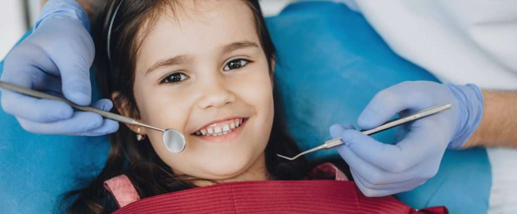 Joven sonriente en el odontólogo, con peto y las manos enguantadas sujetando instrumentos dentales cerca de la boca. de Hospital Dental de Moratalaz "Martínez y Morcuende"