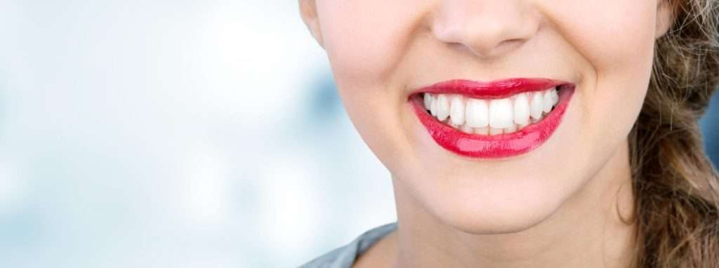 Una mujer con los labios pintados de rojo brillante sonríe, mostrando sus dientes blancos y rectos, perfectos para un anuncio de la clínica dental Moratalaz. de Hospital Dental de Moratalaz "Martínez y Morcuende"
