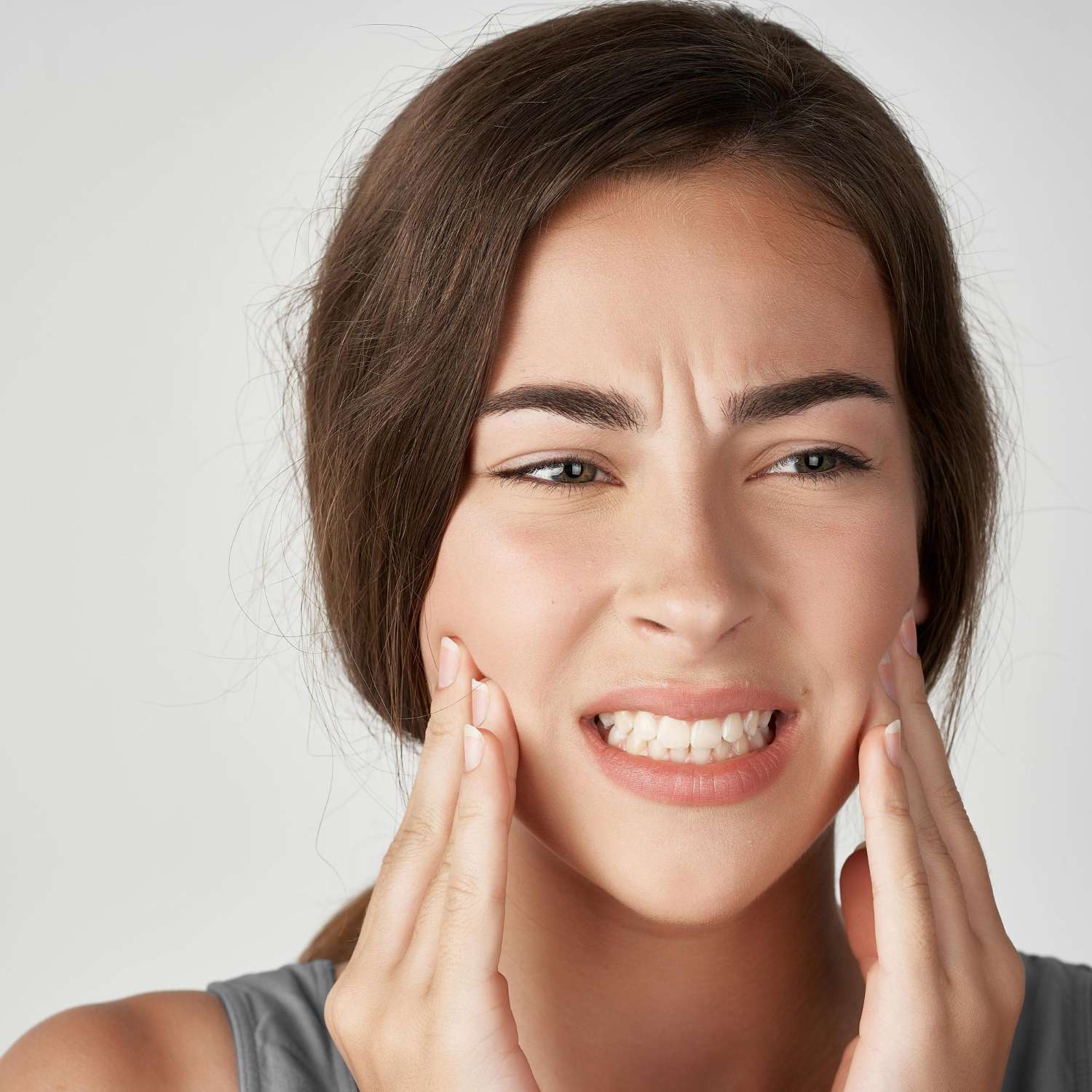 Una mujer de pelo largo y castaño hace una mueca de dolor y sugiere que necesita un dentista en una clínica dental de Moratalaz. de Hospital Dental de Moratalaz "Martínez y Morcuende"